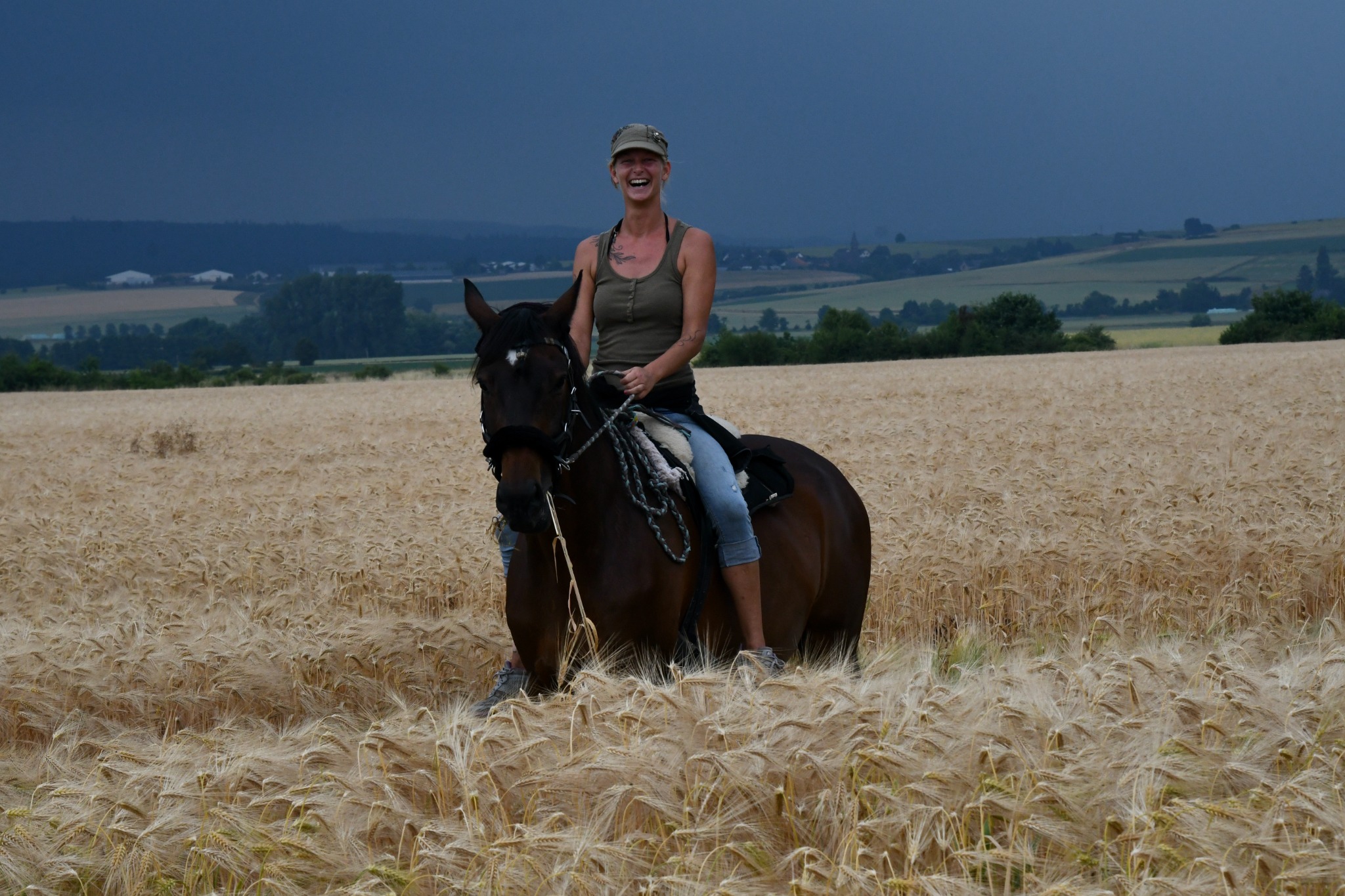 Sabrina Sommer lacht auf ihrem Pferd in einem Kornfeld